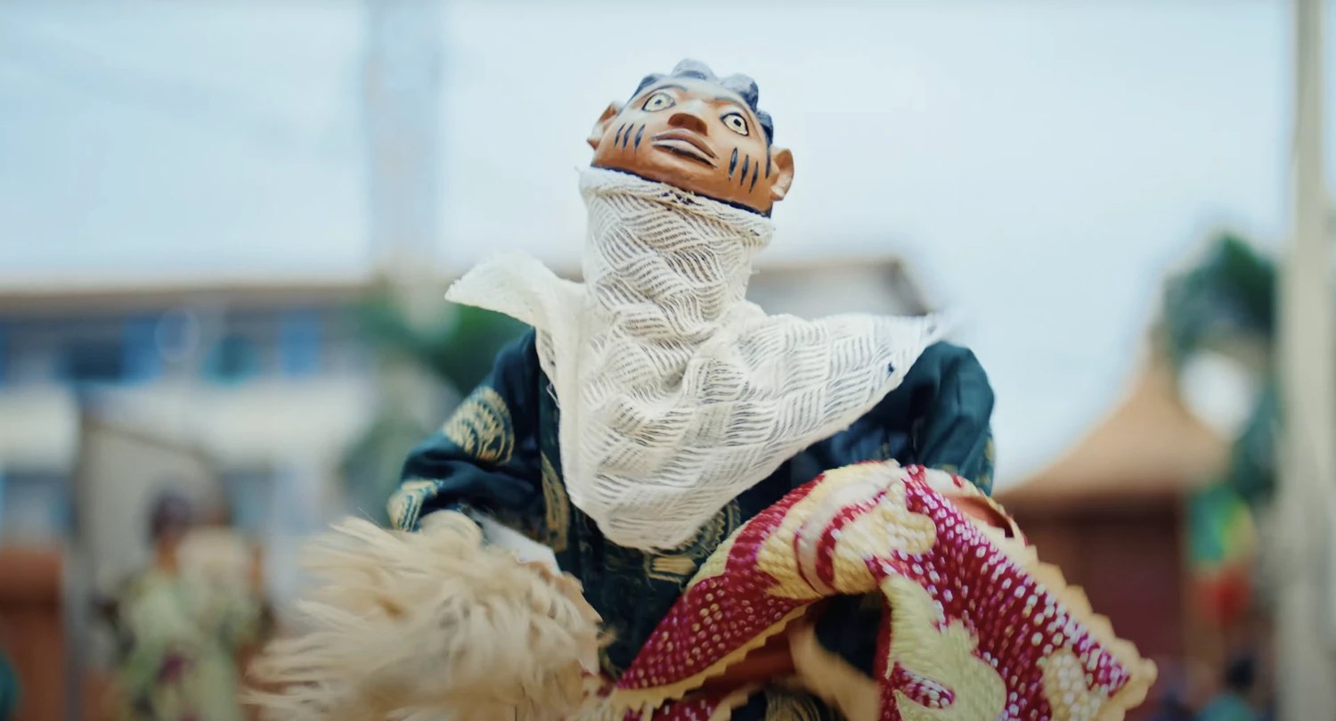 An Egungun masquerade in embroidered cloth, mask raised to the sky